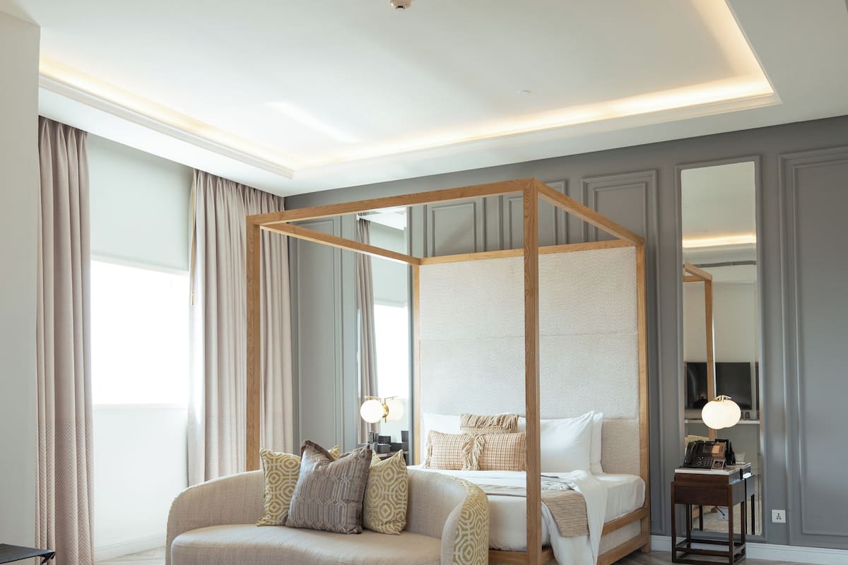 Een moderne slaapkamer met een hemelbed, een bank, een nachtkastje met lamp en een grote spiegel.