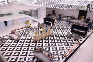 Un vestíbulo moderno con un piso de diseño geométrico, zonas de estar con sofás y sillones, una mesa de centro con objetos decorativos y una barandilla de vidrio con vistas al espacio.