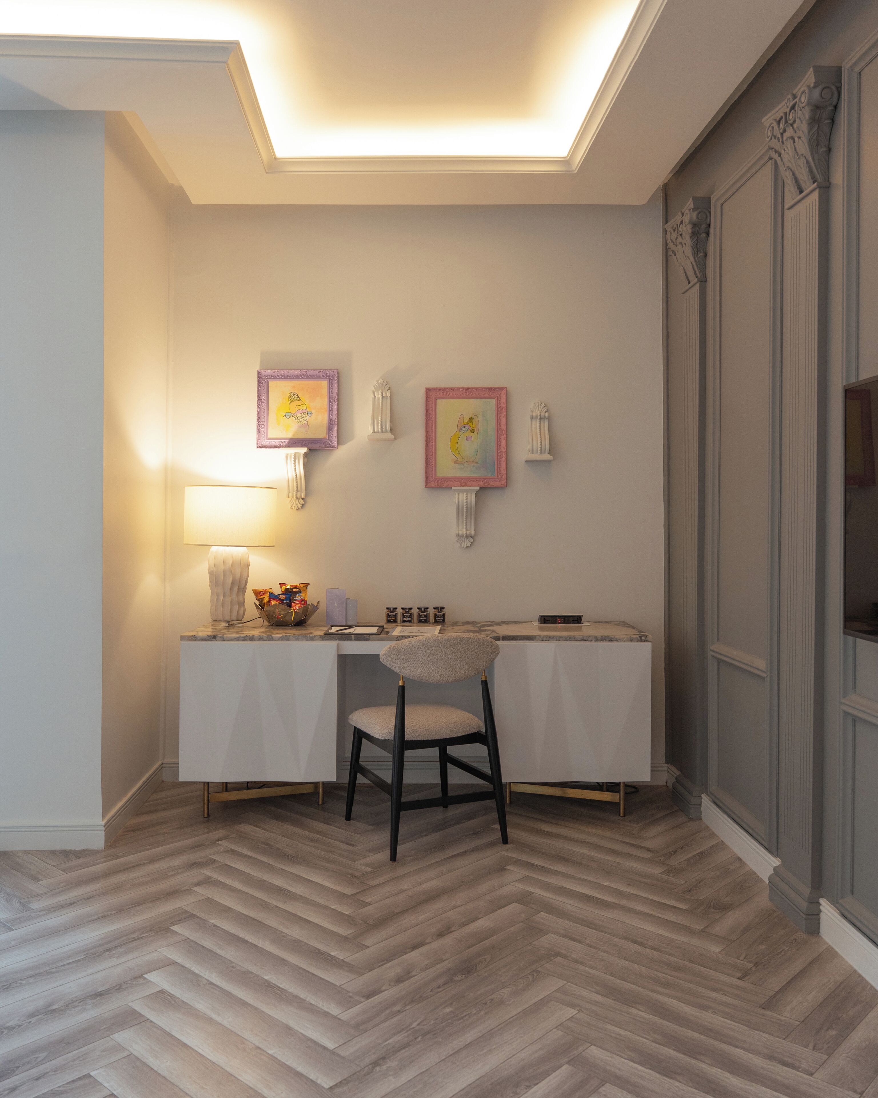 Une pièce comprenant un bureau, une chaise, des lampes fixées au mur et des œuvres d’art encadrées.