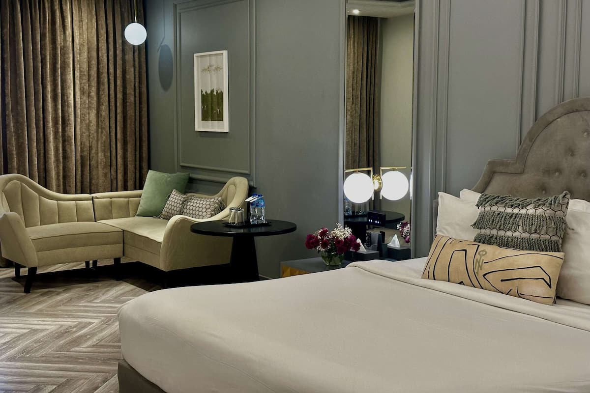 Een hotelkamer met een groot bed, een bank, een kleine tafel met een bloevas en een spiegel.