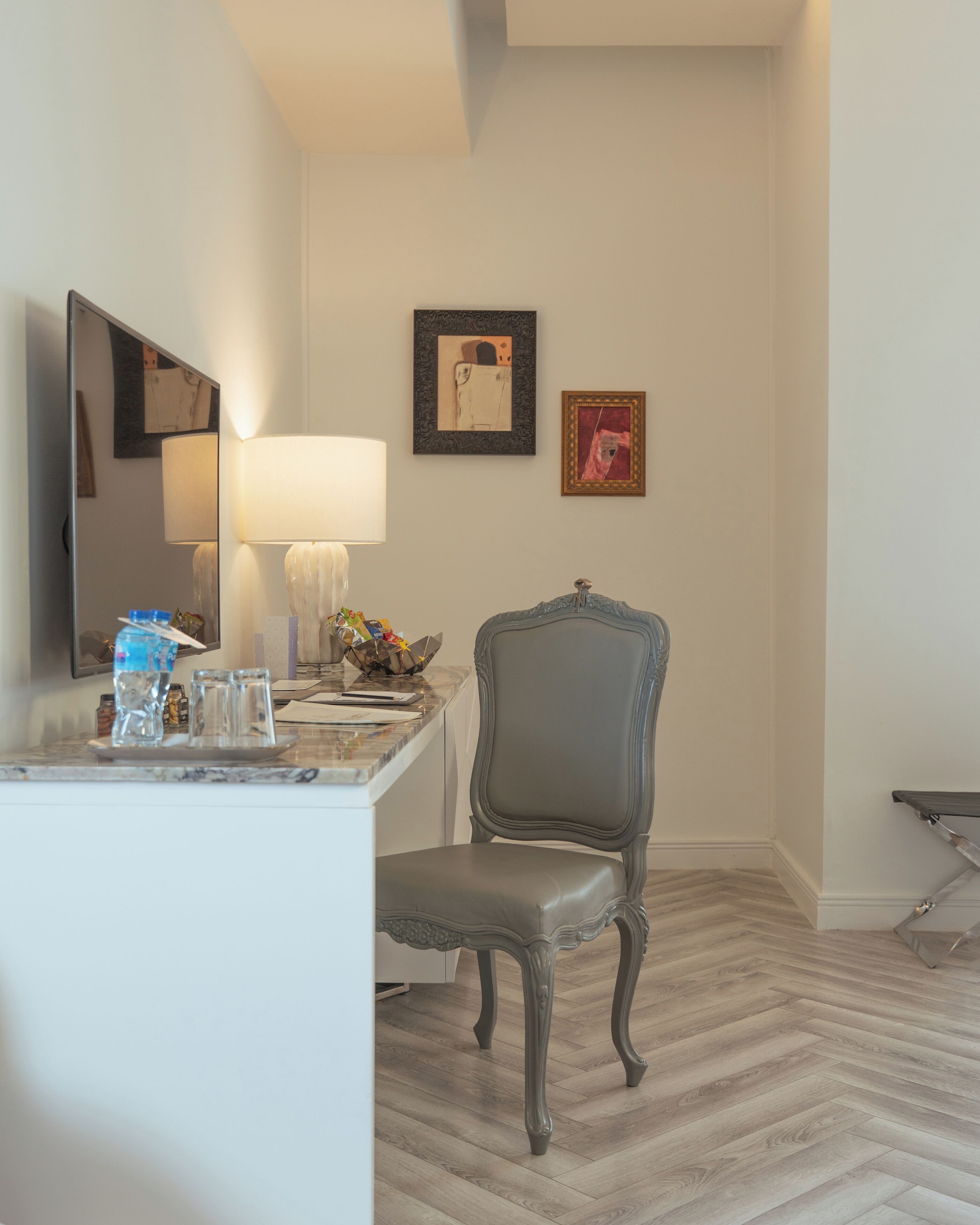 A room with a desk, chair, lamp, and wall art.