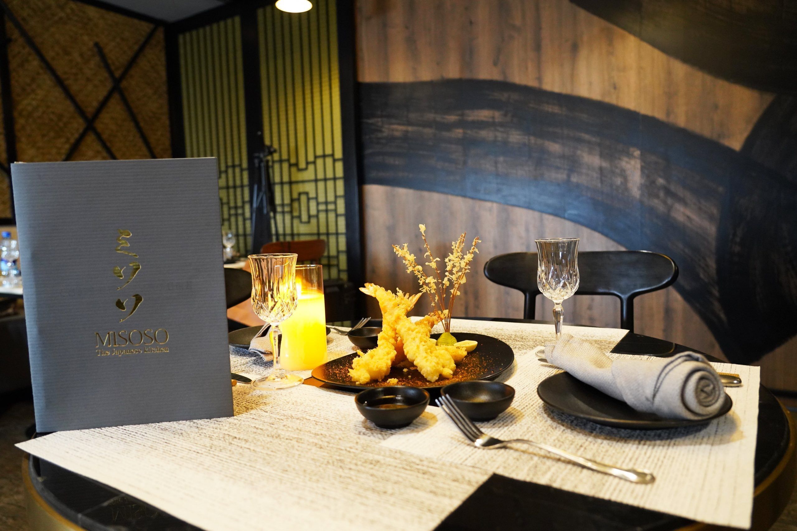 A dining table set with a menu, a glass of water, a glass of wine, and a plate of tempura.