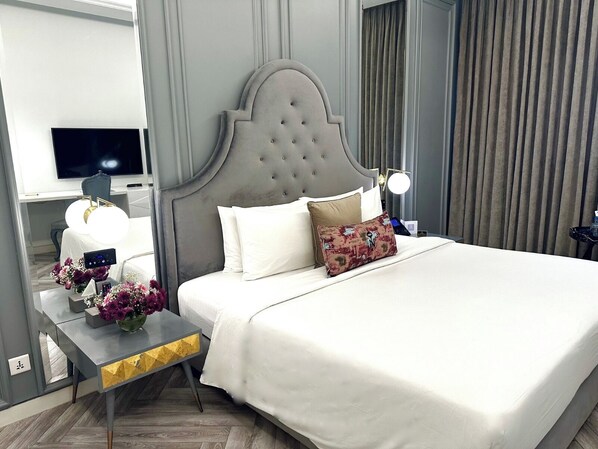 Habitación de hotel con una cama grande, una mesita de noche con lámpara, un televisor y un arreglo floral.