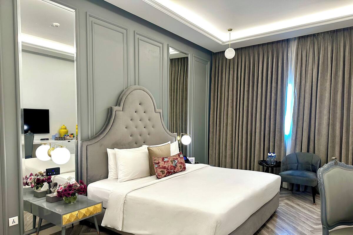 Een moderne hotelkamer met een groot bed, een nachtkastje met lamp, een spiegel en een klein bureau met stoel.