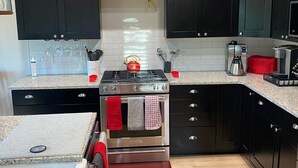 Una cocina moderna con armarios oscuros, una estufa de acero inoxidable y una cafetera.