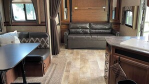A compact RV interior with a kitchenette, a dining area, and a seating area with a sofa and a table.
