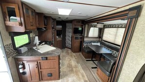 A compact RV kitchen with a central island, built-in appliances, and a seating area with a TV.