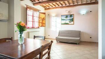 A dining area with a wooden table and chairs, a vase with flowers, a checkered sofa, and a painting of a beach scene.