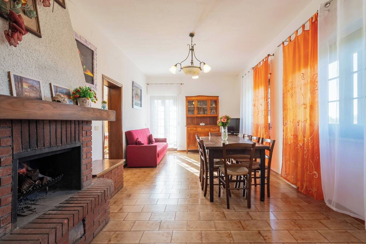 Una sala de estar con chimenea, un comedor con mesa y sillas, una cocina con armarios y un sofá rojo.