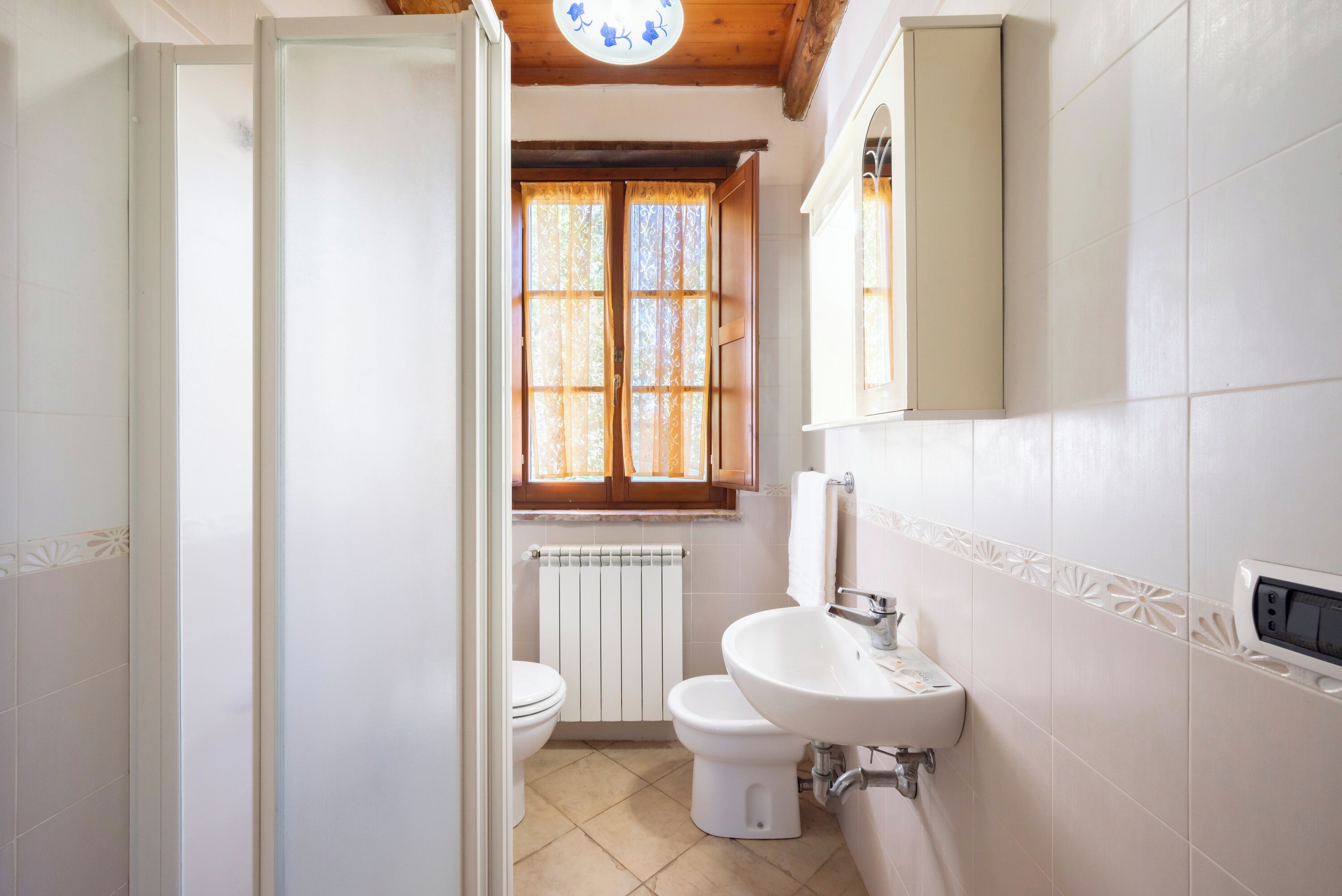 A bathroom with a toilet, sink, and window with curtains.
