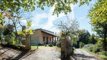 A rustic building with a gravel driveway leading to a gated entrance, surrounded by trees and greenery.
