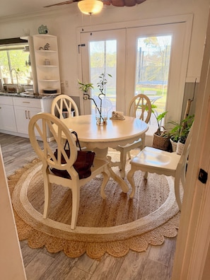 A dining area with a round table, white chairs, a woven rug, and potted plants. - City Center 3b2b Fenced Backyard One Story Home 77041 (Houston)