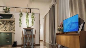 Un salon moderne avec un sol à carreaux, un meuble TV en bois, une table à manger avec des chaises, un buffet vert et des plantes suspendues.