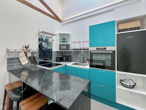 Una cocina moderna con encimera de mármol negro, armarios color turquesa y refrigerador negro.