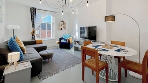 Ett modernt vardagsrum med en soffa, ett soffbord, ett matbord, stolar, en tv och en kristallkrona.