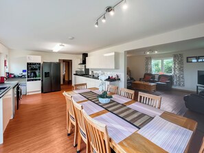 Een moderne keuken met inbouwapparatuur, een eethoek met houten stoelen en een centrale tafel, en een woonkamer met een bank en televisie.