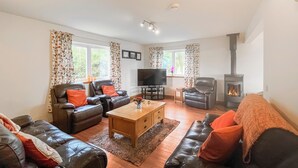A living room with leather sofas, a TV, a fireplace, and a large window. - 4 bedroom accommodation in Southerness (Southerness)