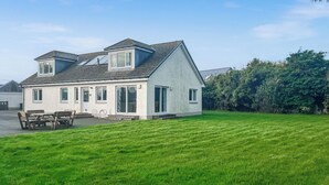 A two-story house with a sloped roof, a front porch with a bench, and a well-maintained lawn. - 4 bedroom accommodation in Southerness (Southerness)