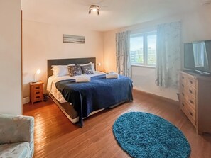 Une chambre à coucher comprenant un lit, une table de chevet, une lampe, une télévision, une commode et une fenêtre avec des rideaux.