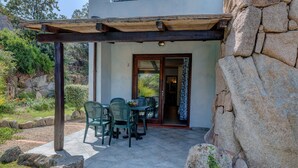 Eine Terrasse mit Tisch und Stühlen, eine Holz-Pergola und eine Steinmauer.