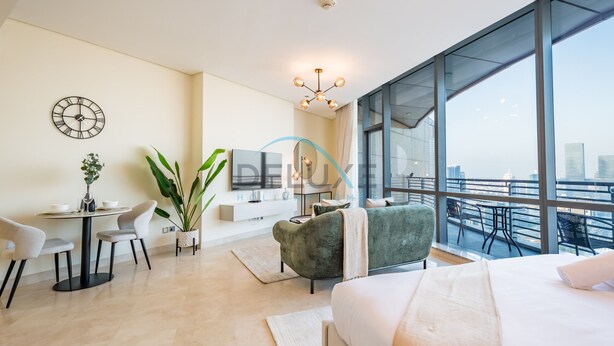 A modern hotel room with a large bed, a desk with chairs, a TV, and a balcony with a city view. - Lively Studio in Sky Gardens, DIFC by Deluxe Holiday Homes (Dubai)