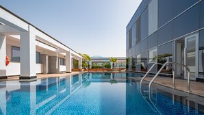 A modern indoor swimming pool with clear blue water, surrounded by contemporary architecture and a clear sky. - Lively Studio in Sky Gardens, DIFC by Deluxe Holiday Homes (Dubai)