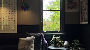 A cozy living room with a dark-colored sofa, a small side table with a plant, and a window with a view of trees. - Deluxe Private Suite in Country Home on 2.6 acres - Daylesford & Hepburn Springs (Daylesford)