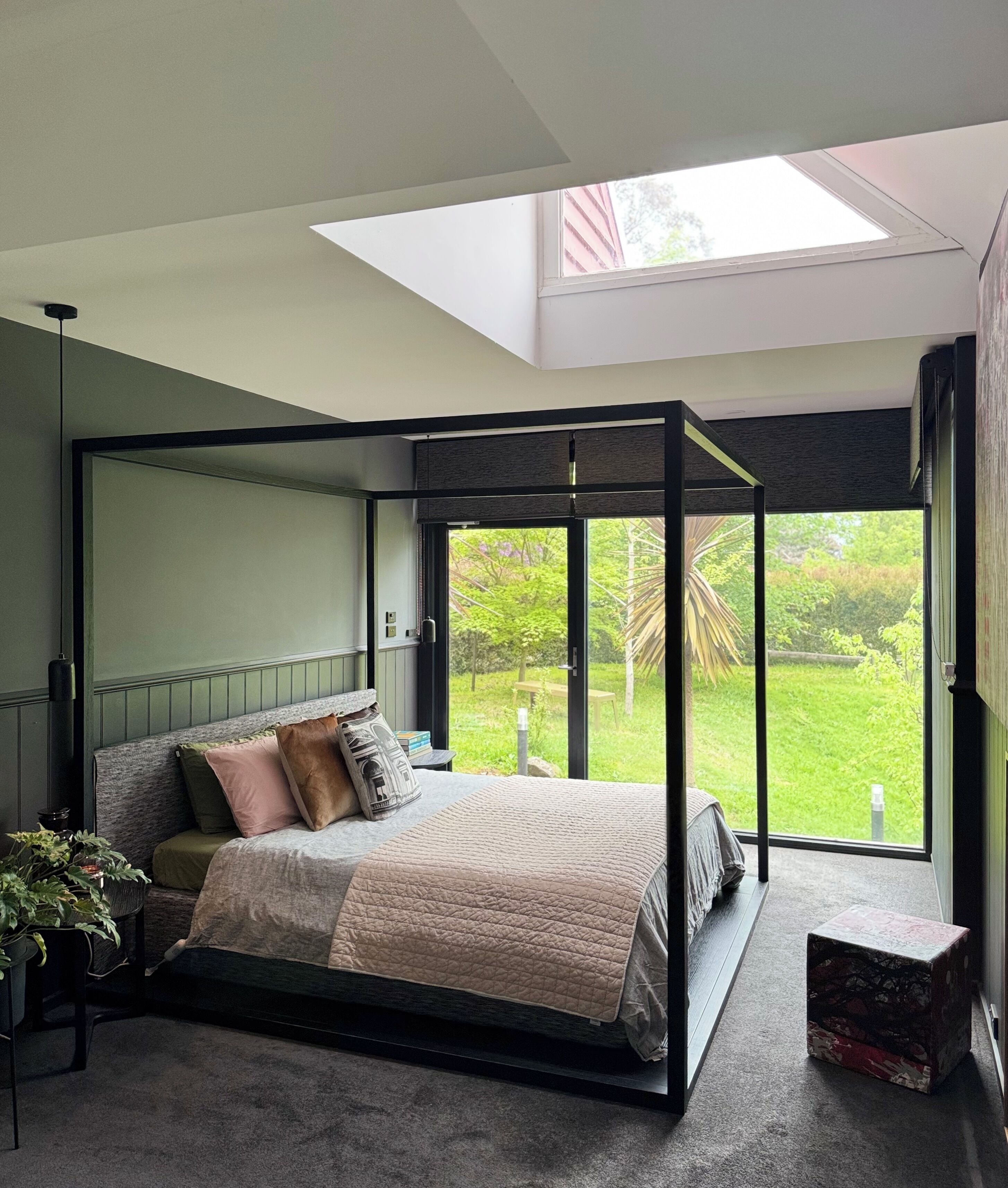 A modern bedroom with a four-poster bed, a skylight, and a view of a garden.