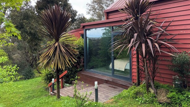 A modern house with a red exterior, a glass door entrance, and a well-maintained garden with large plants. - Deluxe Private Suite in Country Home on 2.6 acres - Daylesford & Hepburn Springs (Daylesford)