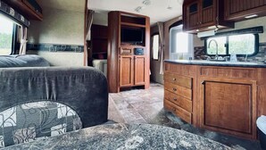 Une cuisine compacte pour camping-car, dotée de meubles en bois, d’un plan de travail en granit et d’un téléviseur intégré.