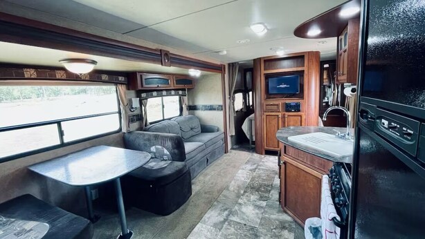 Un intérieur de camping-car compact comprenant un coin cuisine, un espace salon avec un canapé et une table, ainsi qu’un téléviseur.