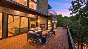 A modern house with a deck, a fireplace, and a staircase leading to the upper floor.