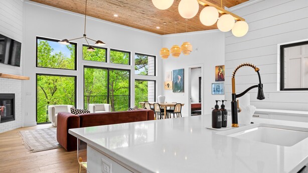 A modern kitchen with a large island, white cabinetry, and a view of the outdoors through large windows. - Heavenly Falls Cabin in Broken Bow | Waterfall Retreat (Broken Bow)