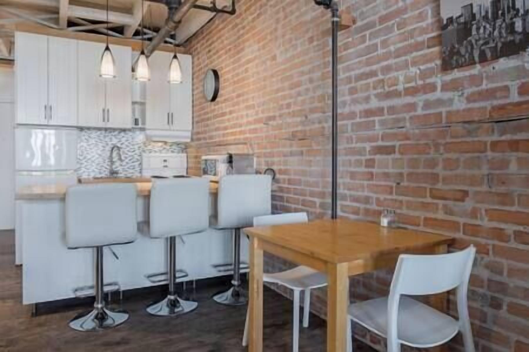 A modern kitchen with white cabinets, a brick wall, and a wooden table with four bar stools.
