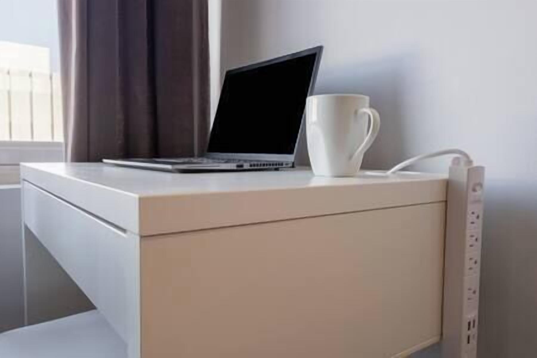 Un ordinateur portable est posé sur un bureau blanc, avec une tasse blanche à côté.