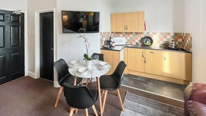 Een compacte keuken met een eethoek, met een televisie, magnetron en houten kastjes.