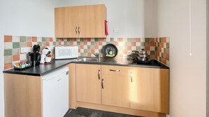 Een kleine keuken met houten kastjes, een witte vaatwasser, een magnetron en een koffiezetapparaat.
