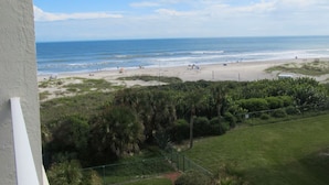 Une vue sur la plage depuis un balcon, avec un ciel dégagé, une plage de sable et une végétation luxuriante.