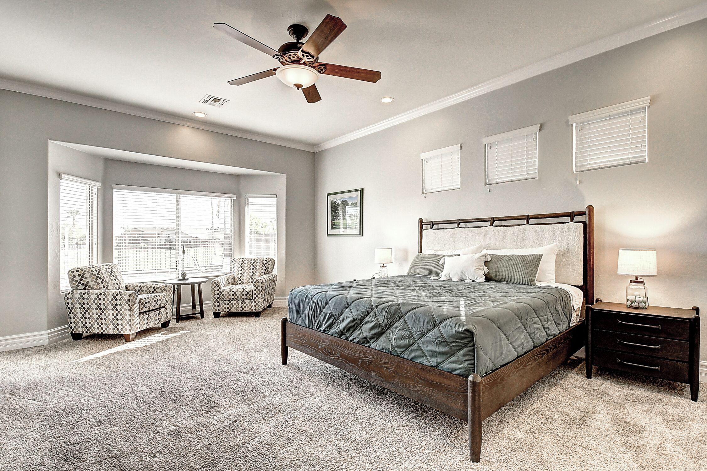 A bedroom with a large bed, a ceiling fan, and a window with blinds.