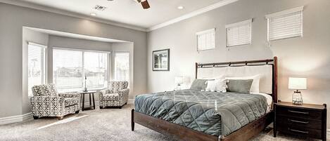 A bedroom with a large bed, a ceiling fan, and a window with blinds.