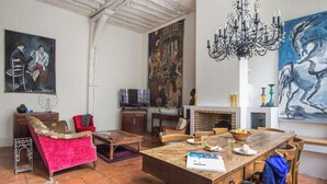 A spacious living room with a wooden dining table, red sofa, and a large painting on the wall. - A TRUE PARISIAN DUPLEX IN THE HEART OF PARIS - MARAIS - RUE DE LA VERRERIE (Paris)