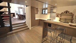 A modern kitchen with a central island, a dining area with a chandelier, and a staircase leading to another level. - A TRUE PARISIAN DUPLEX IN THE HEART OF PARIS - MARAIS - RUE DE LA VERRERIE (Paris)
