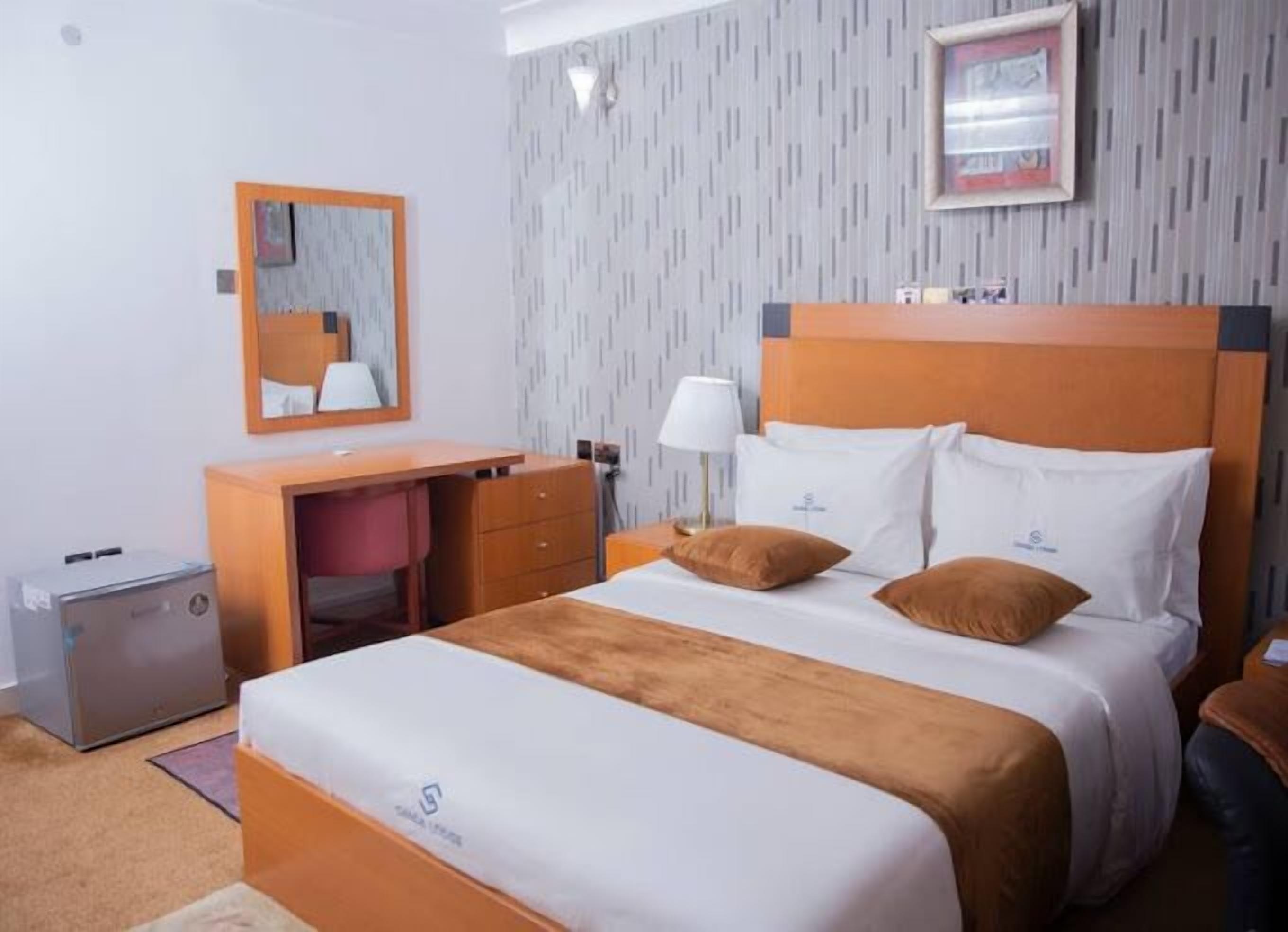 Une chambre d’hôtel avec un lit, un bureau, une chaise, une lampe et une poubelle.