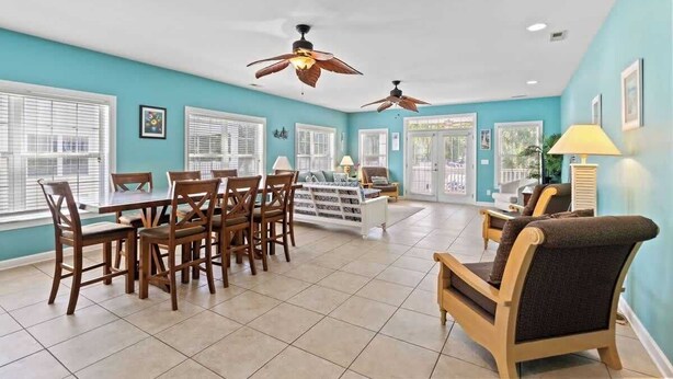 A spacious room with a dining table, chairs, a sofa, and two ceiling fans.