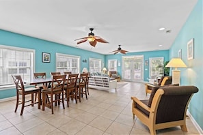 A spacious room with a dining table, chairs, a sofa, and two ceiling fans.