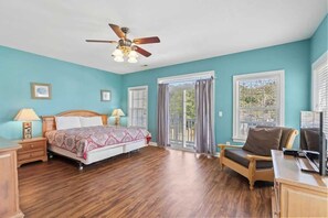 A bedroom with a bed, a desk, a chair, a ceiling fan, and a window with curtains.