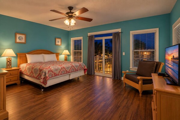 A hotel room with a bed, a desk with a chair, a television, and a ceiling fan.