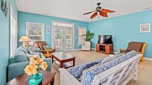 A living room with a sofa, armchairs, a coffee table, a TV, and a ceiling fan.