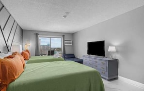 Habitación de hotel con dos camas, un televisor, un aparador y una ventana con vista a la ciudad.