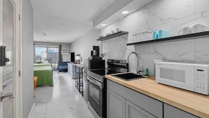 Une cuisine moderne équipée d’un four à micro-ondes, d’une cuisinière et d’un évier, avec vue sur une chambre dont le lit est recouvert d’une courtepointe verte.
